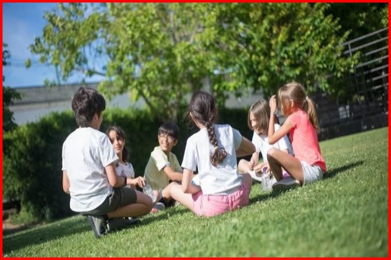 Group of children sitting in a circle on the grass, enjoying outdoor play and social interaction in a park or school playground.